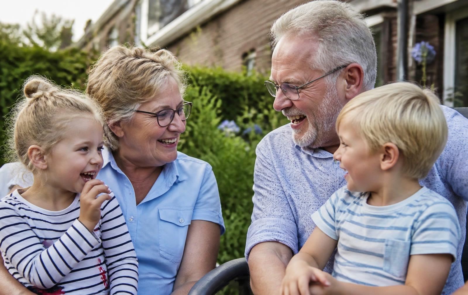 Opa en oma van rond de zestig lachen samen met hun twee kleinkinderen in de tuin